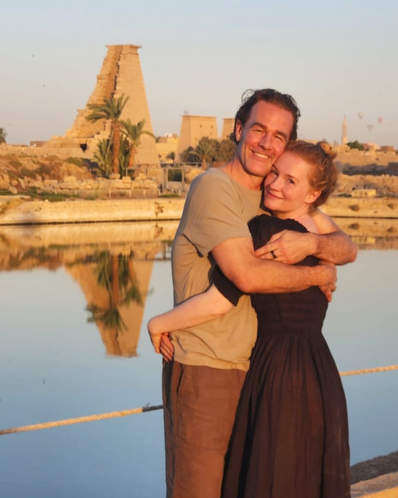 James Van Der Beek and his wife, Kimberly Brook, embracing with an ancient Egyptian temple and palm trees in the background, reflected in the water.
