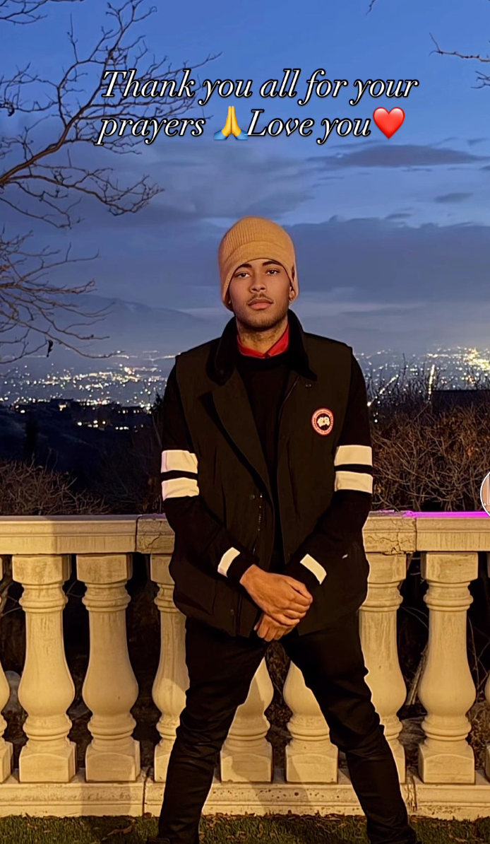 Robert Jr. poses in a beanie and vest with an urban landscape at night behind him.