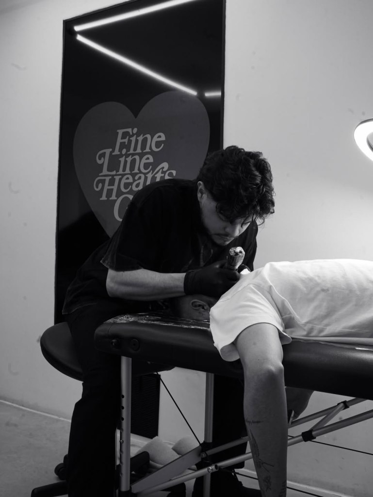 A man giving a tattoo to Romeo Beckham.