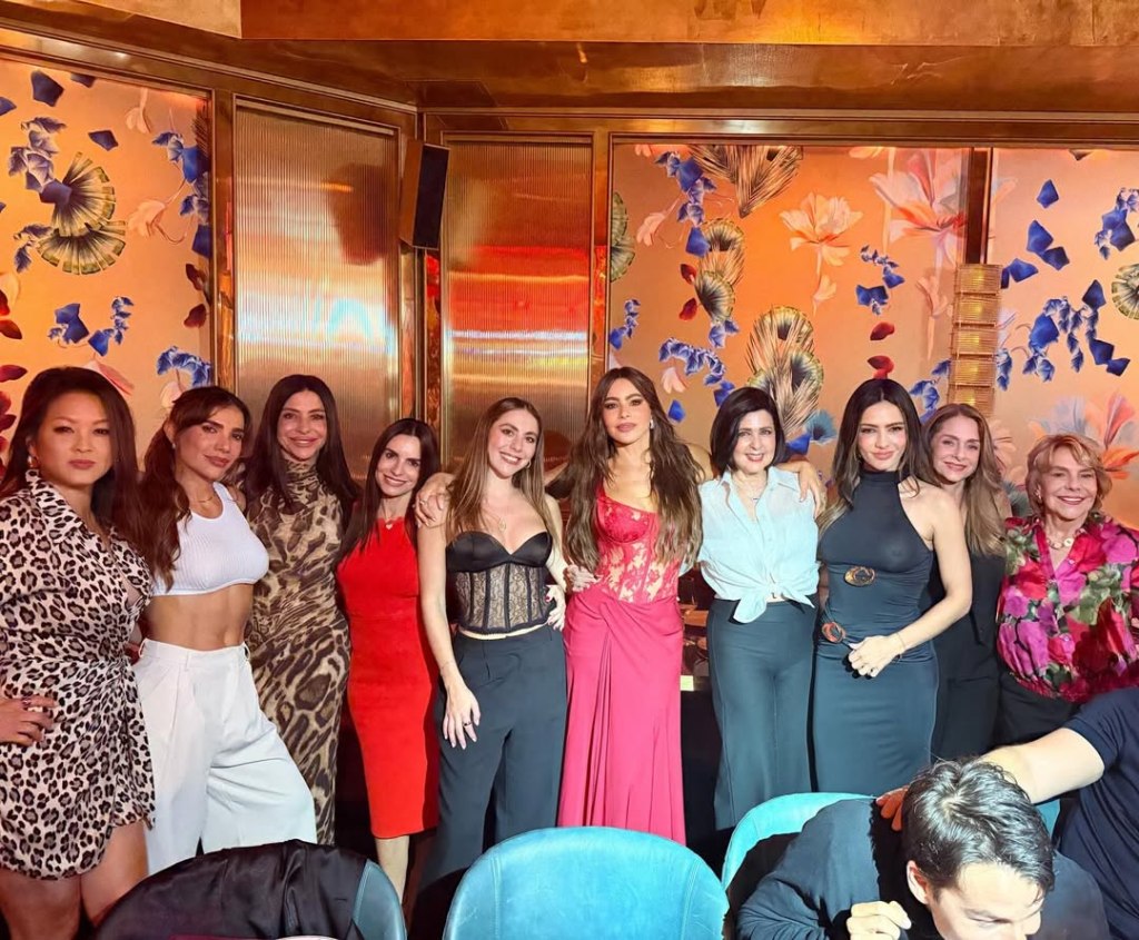 Sofia Vergara in a plunging red dress posing with a group of women.