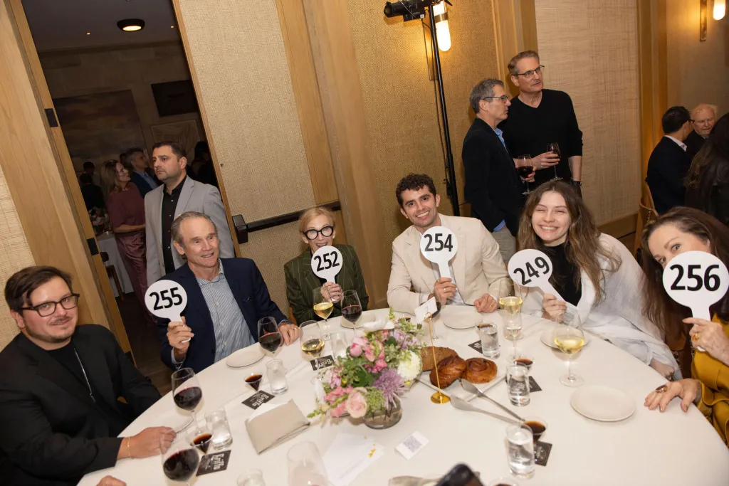 Catherine O'Hara at a table holding up white paddles with numbers for an auction.