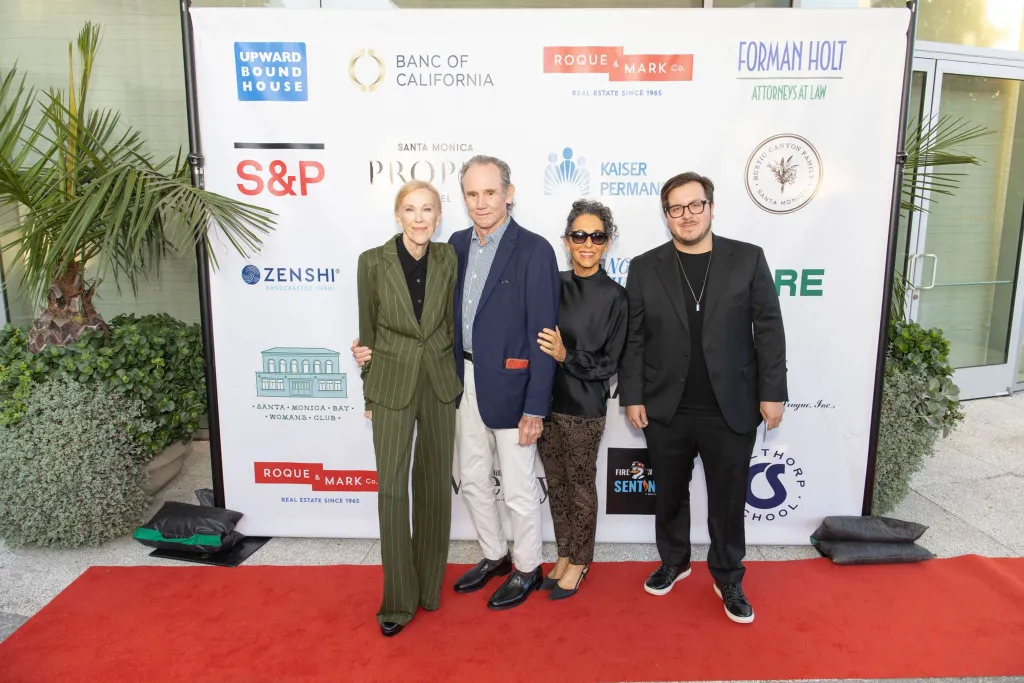 Catherine O'Hara and three other people pose for a photo on a red carpet in front of a white banner with sponsor logos.