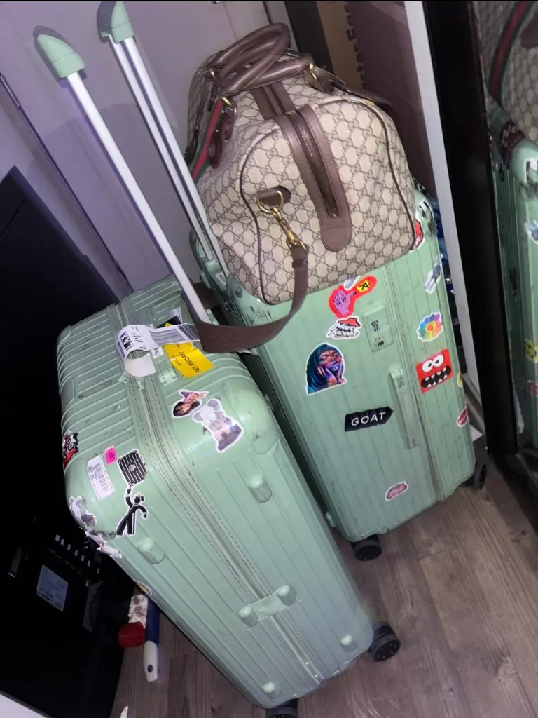 Two light green suitcases, covered in stickers, one with a Gucci duffel bag on top, show visible damage.