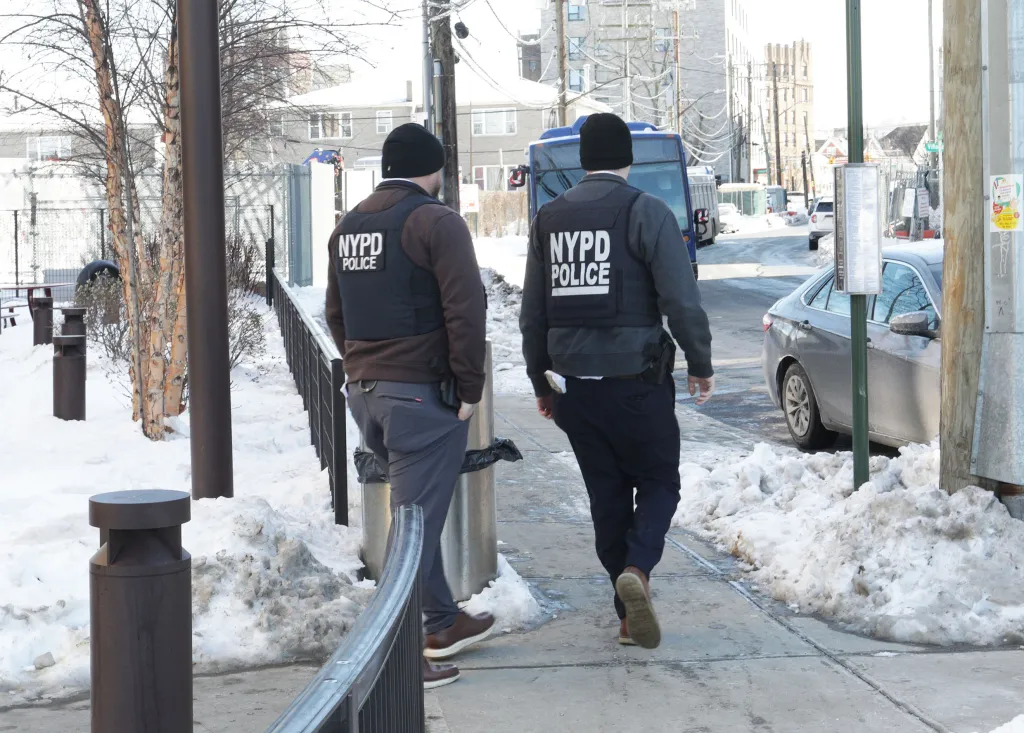 Two NYPD officers walking on a snow-covered sidewalk.