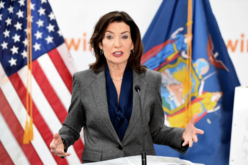 Kathy Hochul speaking at a podium with US and New York state flags behind her.