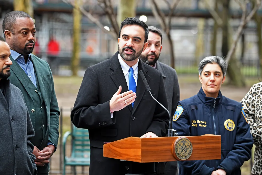 NYC Mayor Zohran Mamdani speaking at a podium with Deputy Mayor Lila Bozorg beside him.