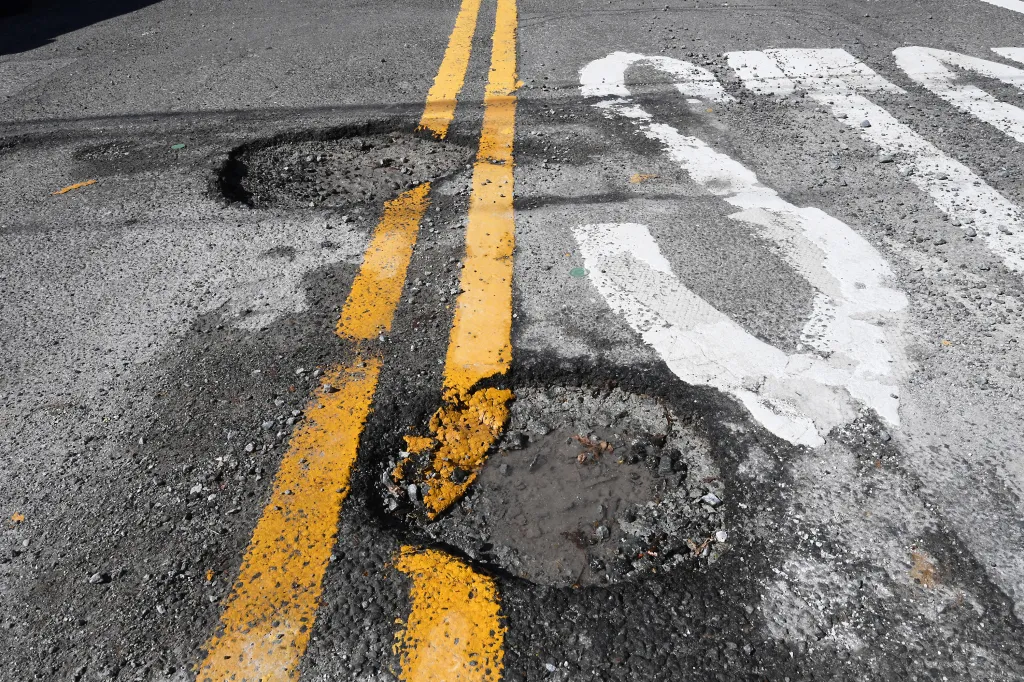 A road with two yellow lines and two potholes.