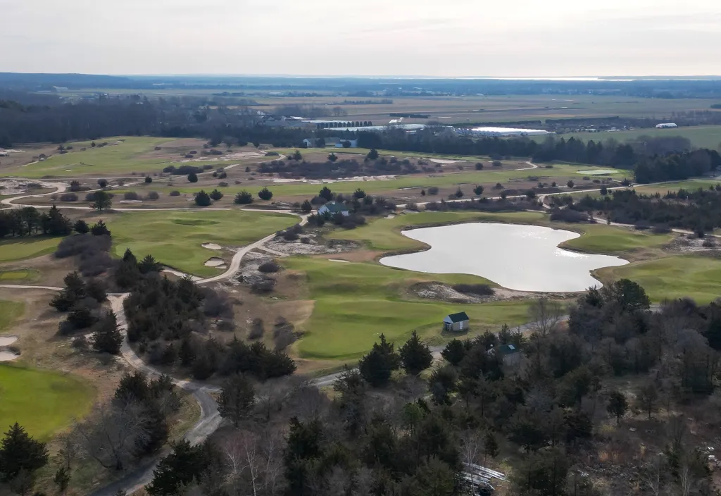 Aerial view of Friar's Head golf course in Riverhead, New York, featuring green fairways, sand traps, a lake, and surrounding trees.