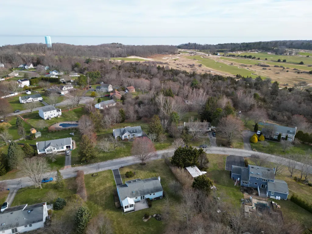 Aerial view of Friar's Head golf course in Riverhead, NY, with residential homes in the foreground and a water tower in the distance.