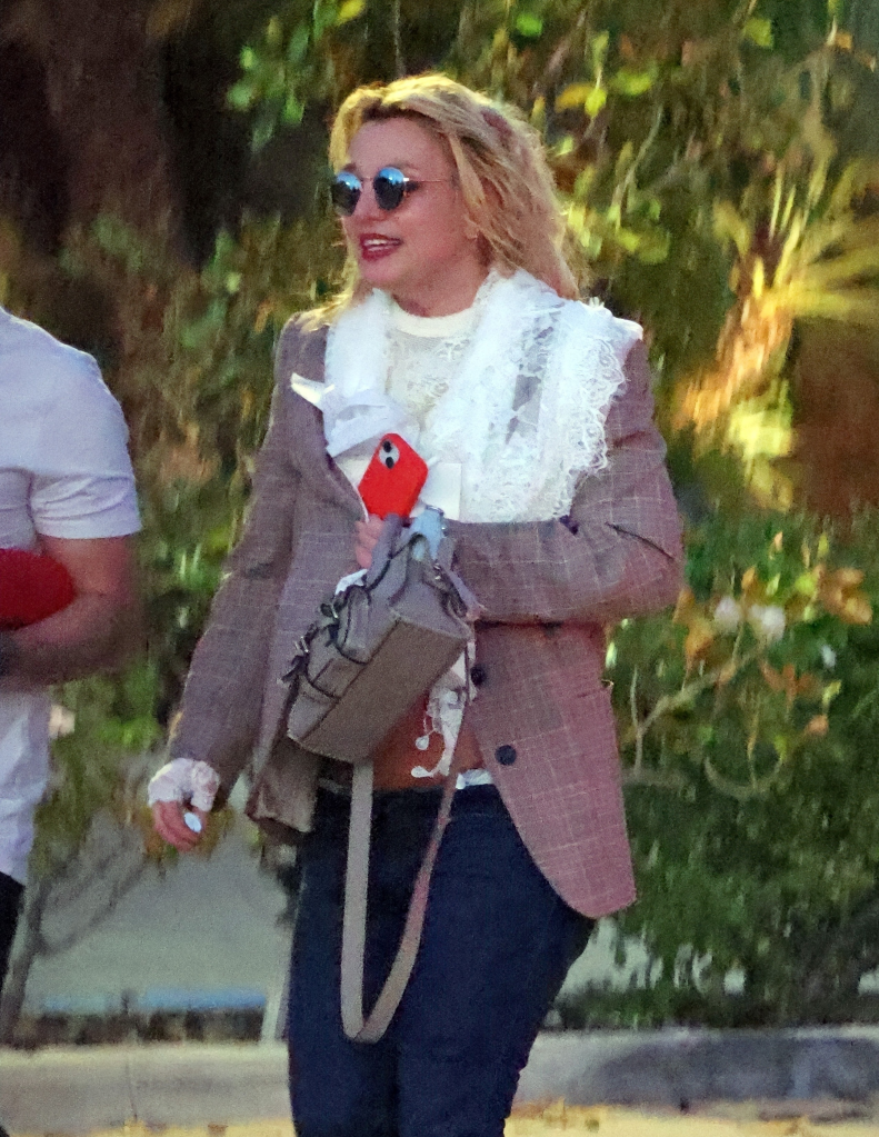 Britney Spears in a blazer, sunglasses, and carrying a handbag and phone.