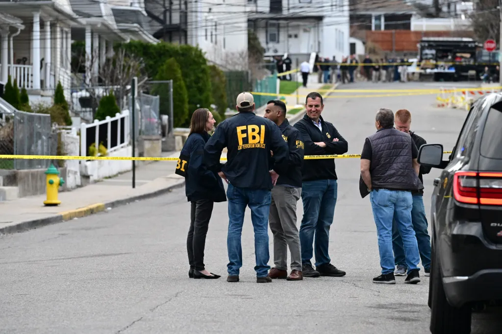 FBI agents and law enforcement gather at a crime scene blocked off by yellow police tape.