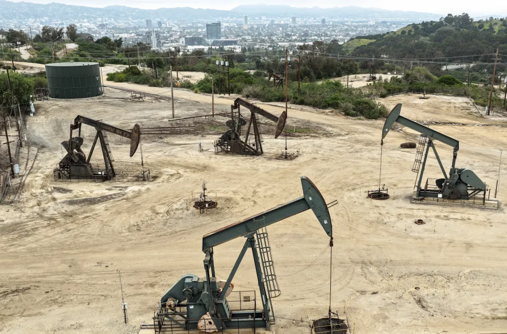 Aerial view of several active and idle oil pumpjacks in the Inglewood Oil Field with the Los Angeles skyline in the background.