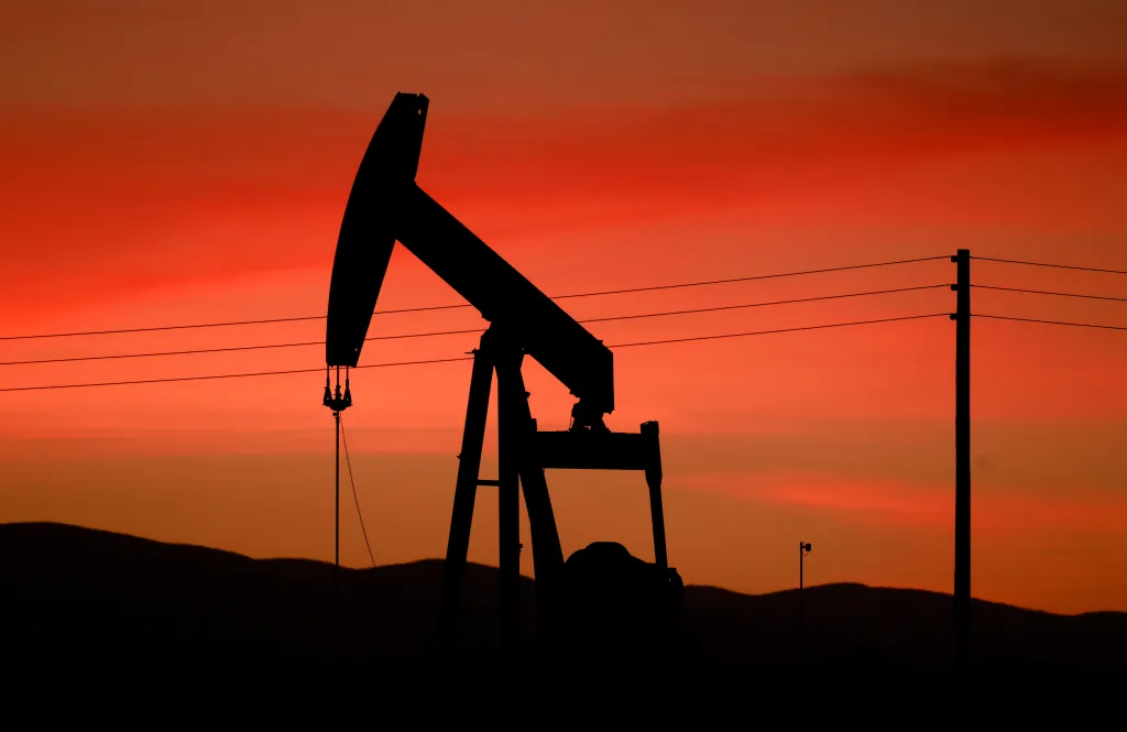 A pumpjack is silhouetted against an orange sunset sky.