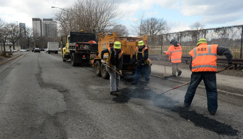Pothole repair crew with a yellow truck and tar spreading asphalt on a road.