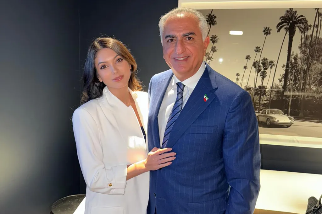 A woman in a white blazer with a hand on the arm of a man in a blue suit with an Iranian flag pin.