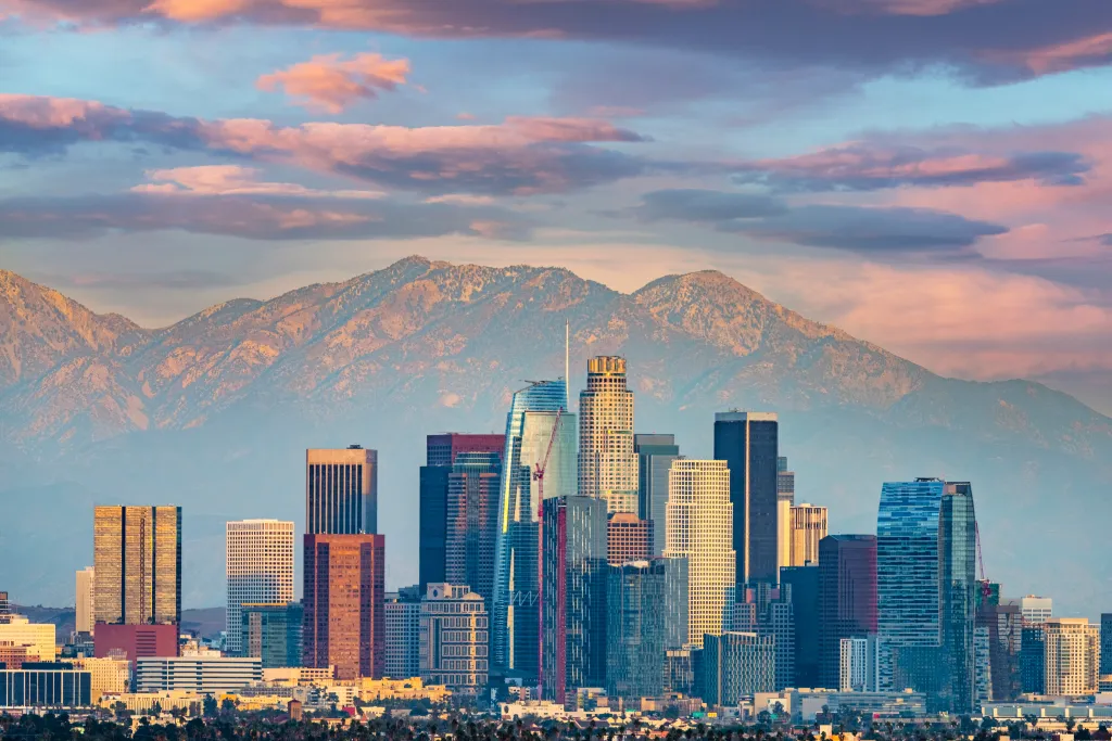 Los Angeles cityscape at dusk with mountains and pink clouds.