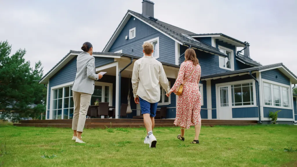 Female real estate agent with a tablet showing a blue house to a couple.