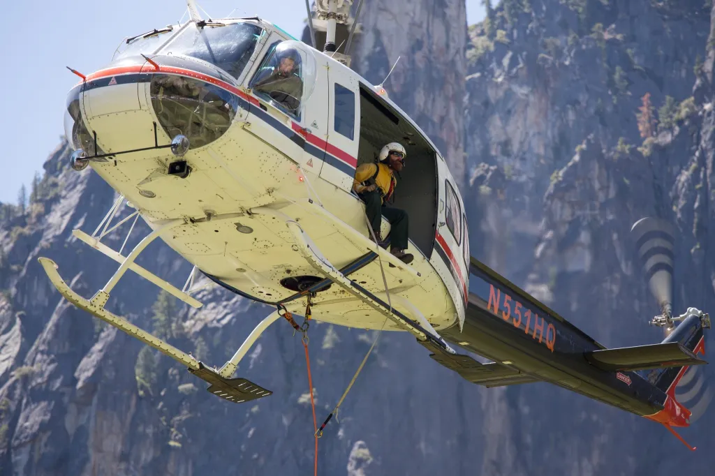 A firefighter sitting in the doorway of a U.S. Wildland Fire Service helicopter over a canyon.