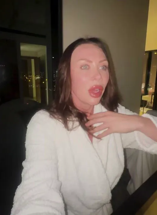 Woman in a bathrobe, with her mouth agape and her hand on her chest, looks surprised.