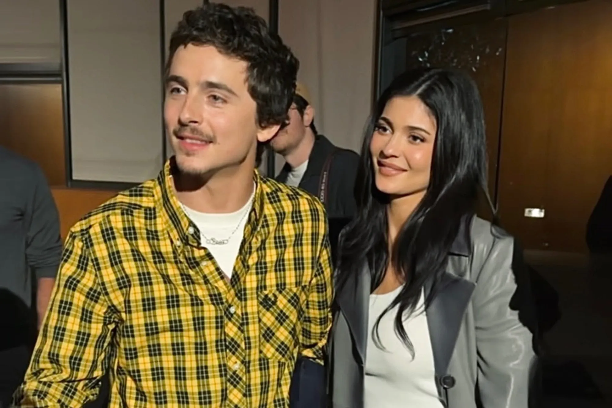 A young man in a yellow plaid shirt and a young woman with long dark hair, both smiling.