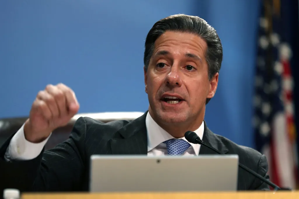 Man in a suit making a fist and speaking into a microphone.