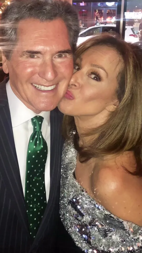 A woman in a sparkly silver dress kisses a man in a pinstripe suit and polka dot tie on the cheek.