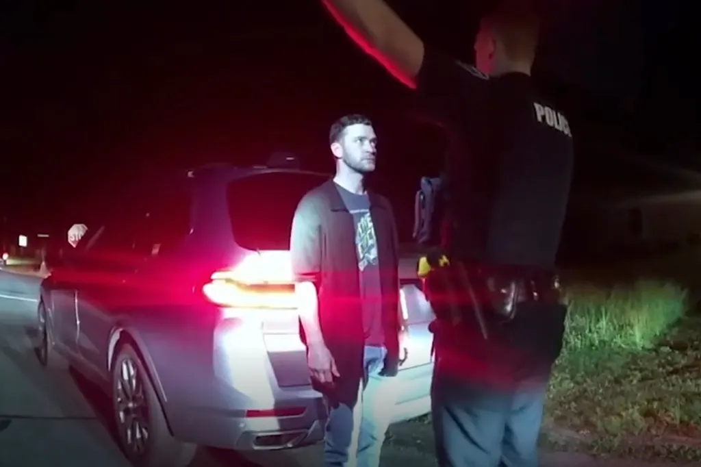 Police officer conducting a field sobriety test on a man in front of a car at night.