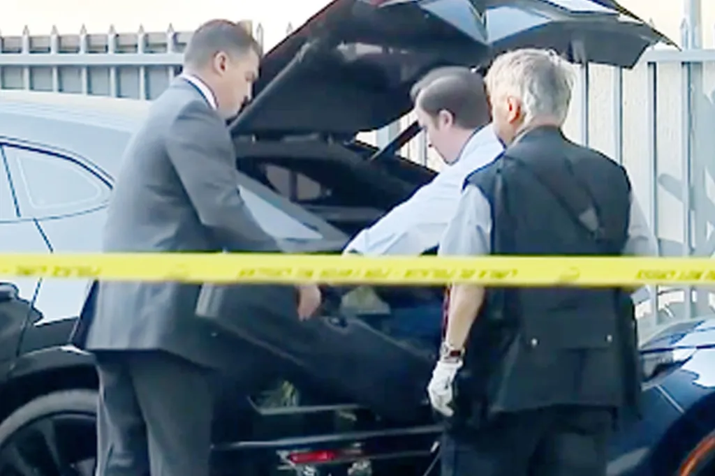 Investigators examining the trunk of a black car behind yellow police tape.