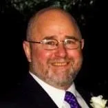 Headshot of a smiling bald man with a beard and glasses, wearing a suit and patterned tie.