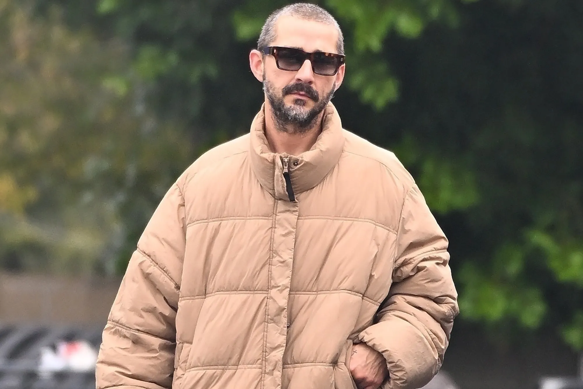 Shia LaBeouf in a tan puffer jacket and sunglasses.