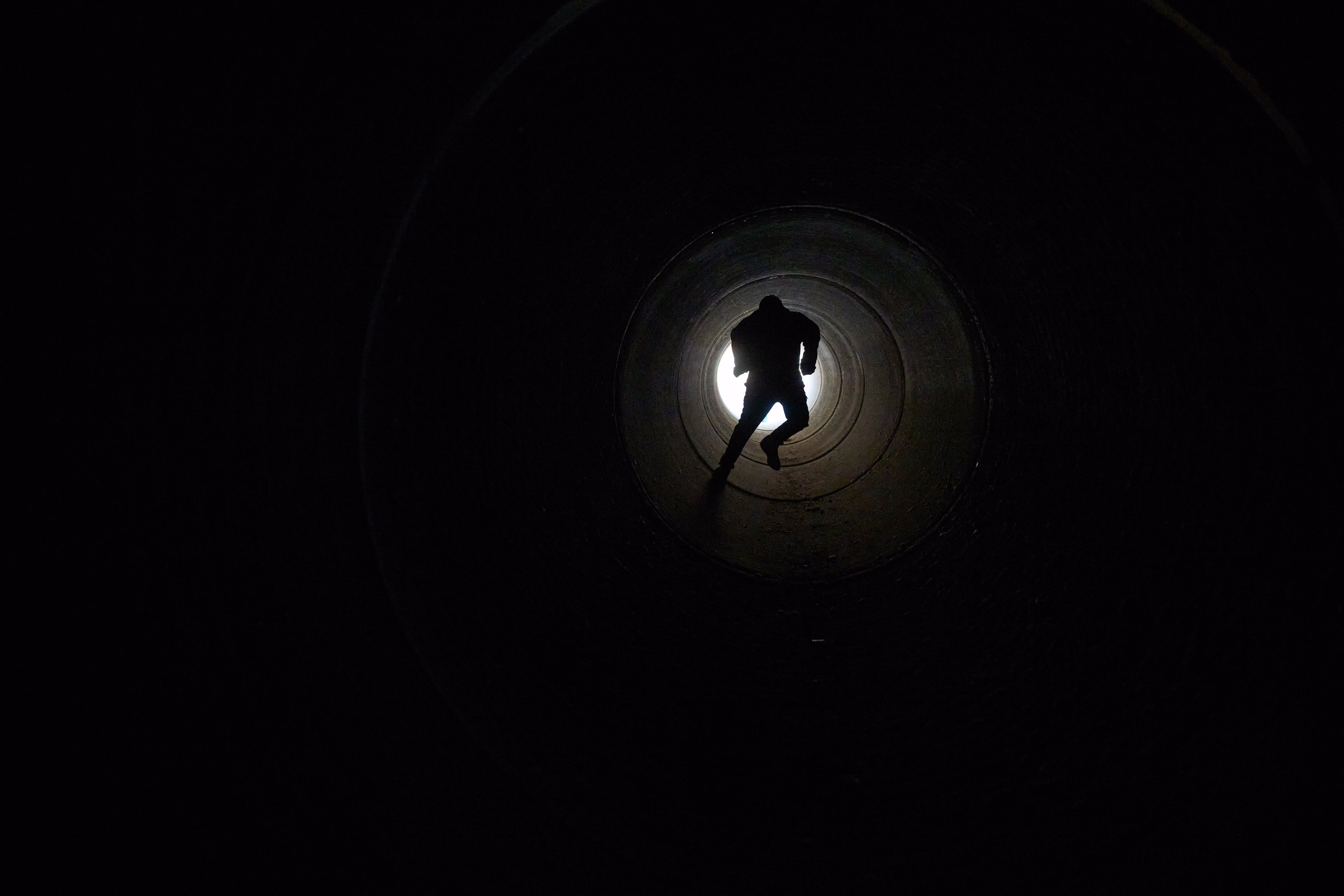 A boy runs inside a large cement pipe, seen from inside.