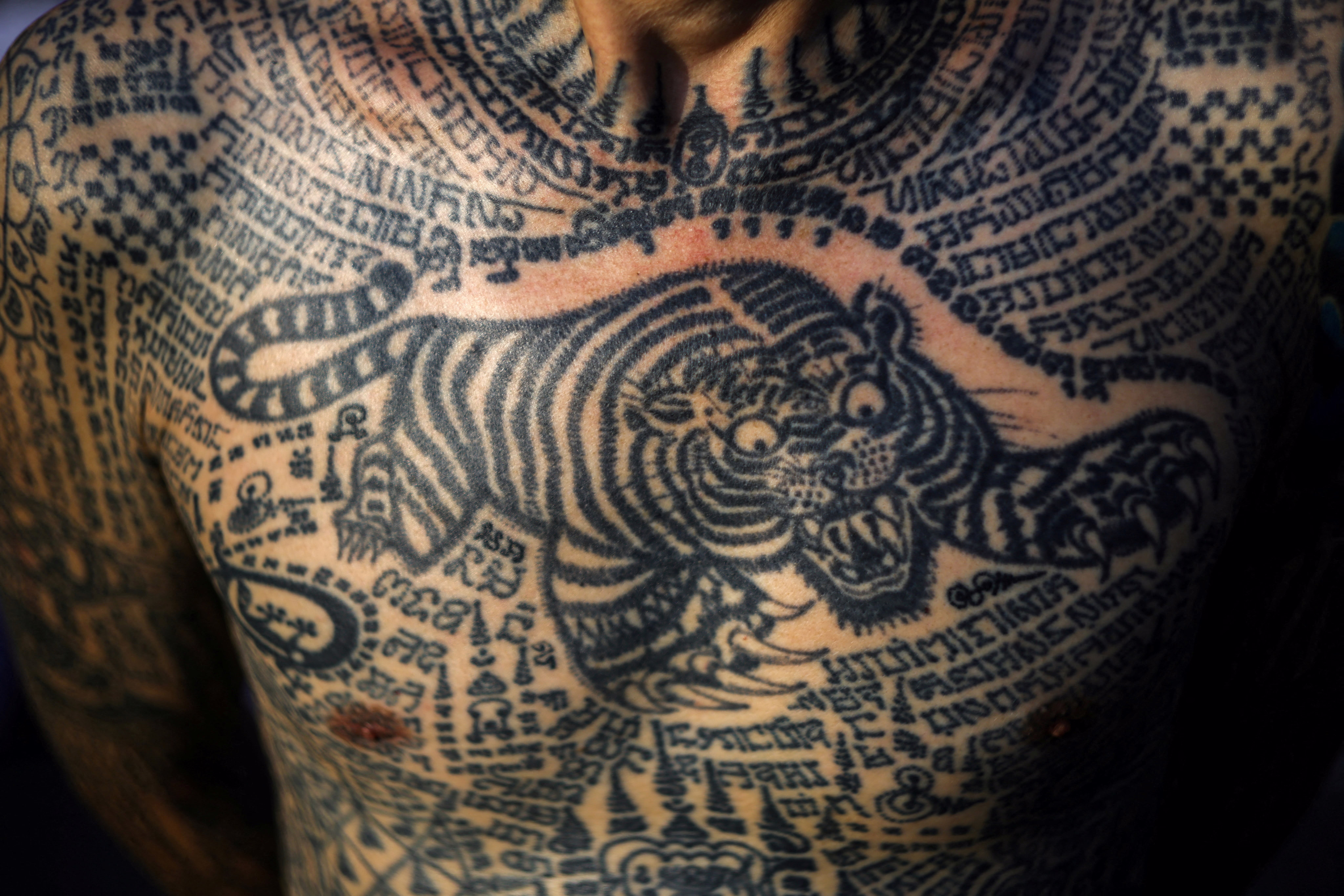 A close photo of a person's chest covered in many detailed tattoos, most prominently a stylized tiger.
