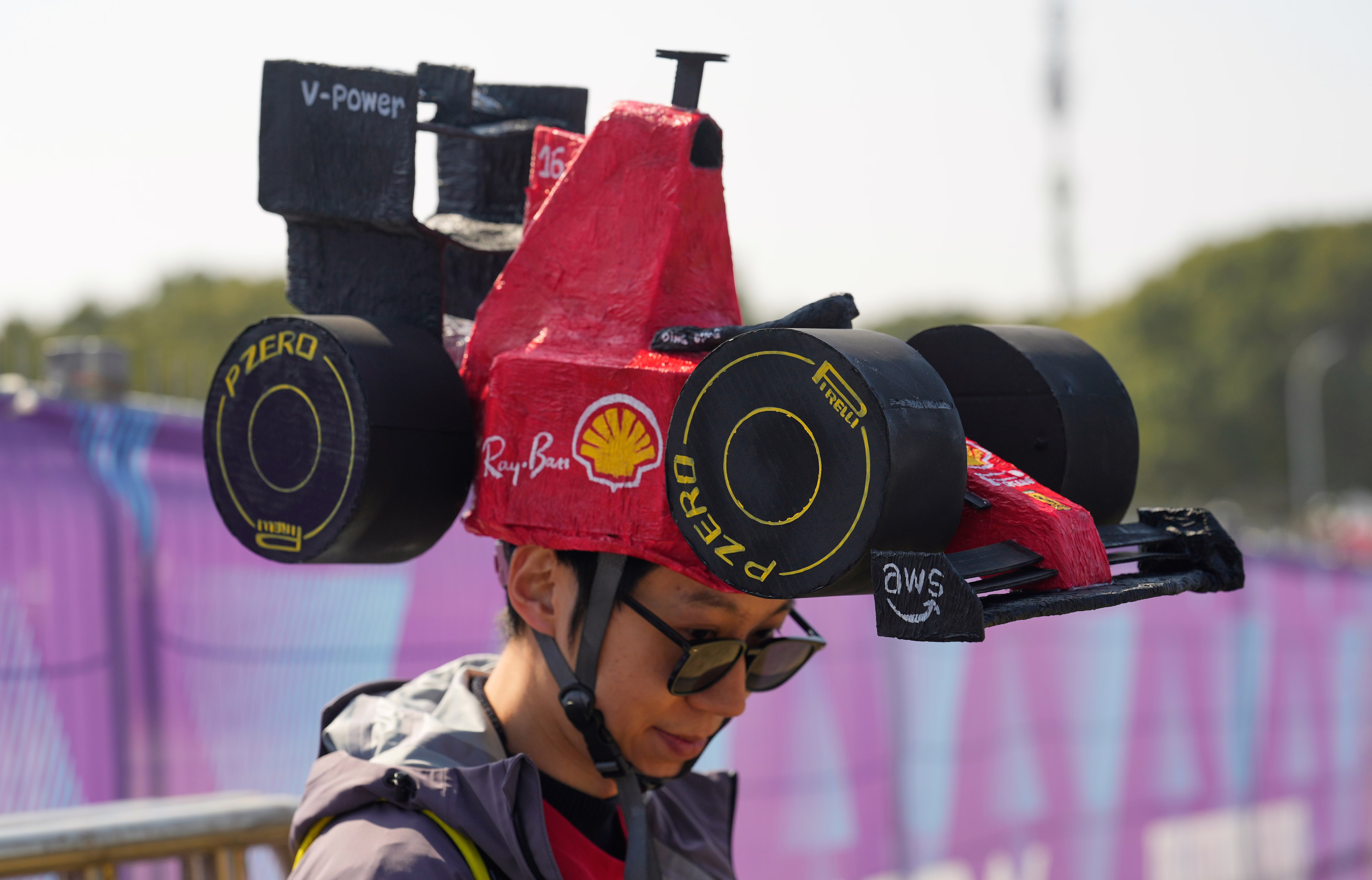 A racing fan wears a large hat shaped like an F1 race car.