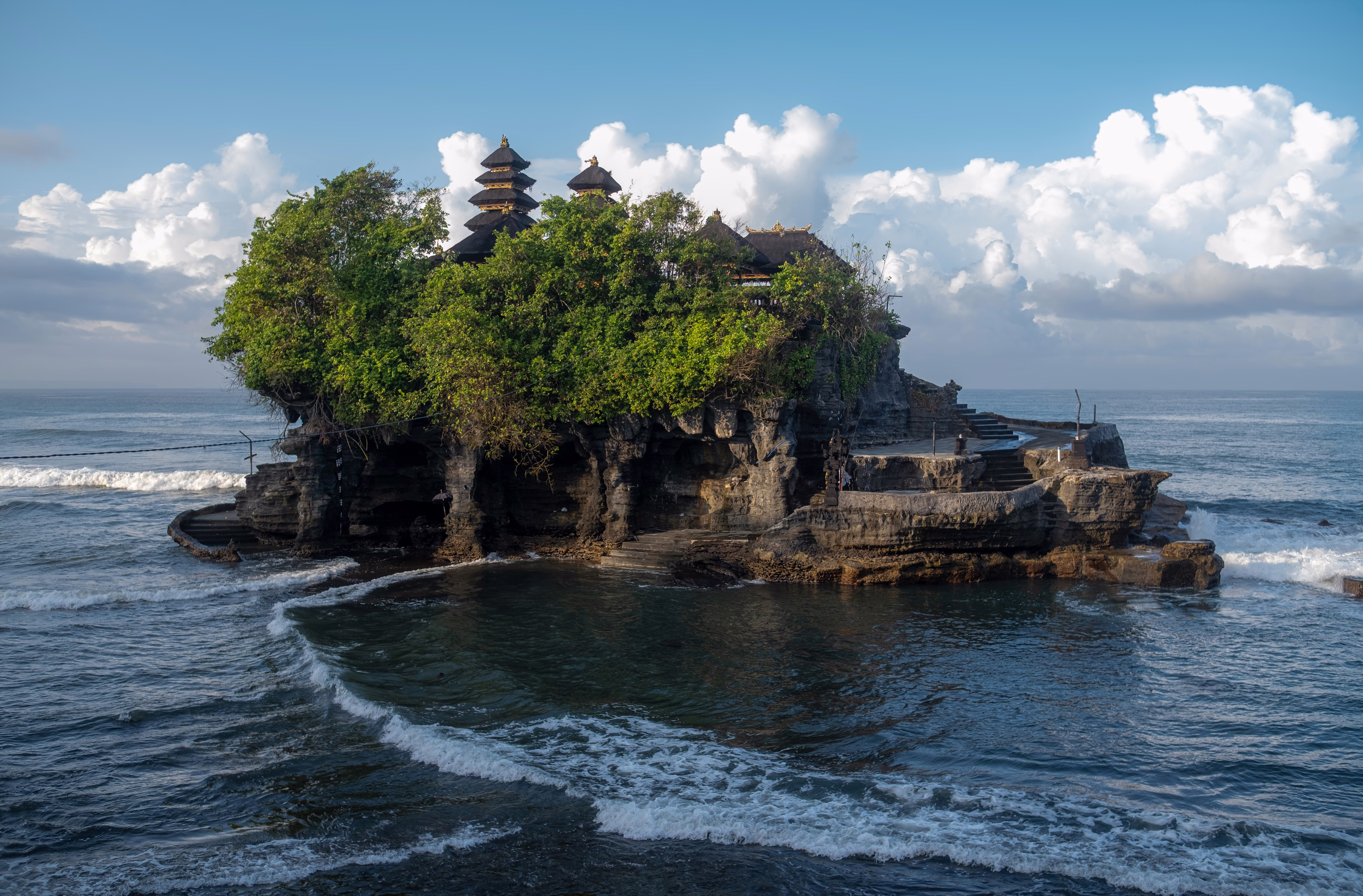 A temple sits atop a small rocky island, just offshore.