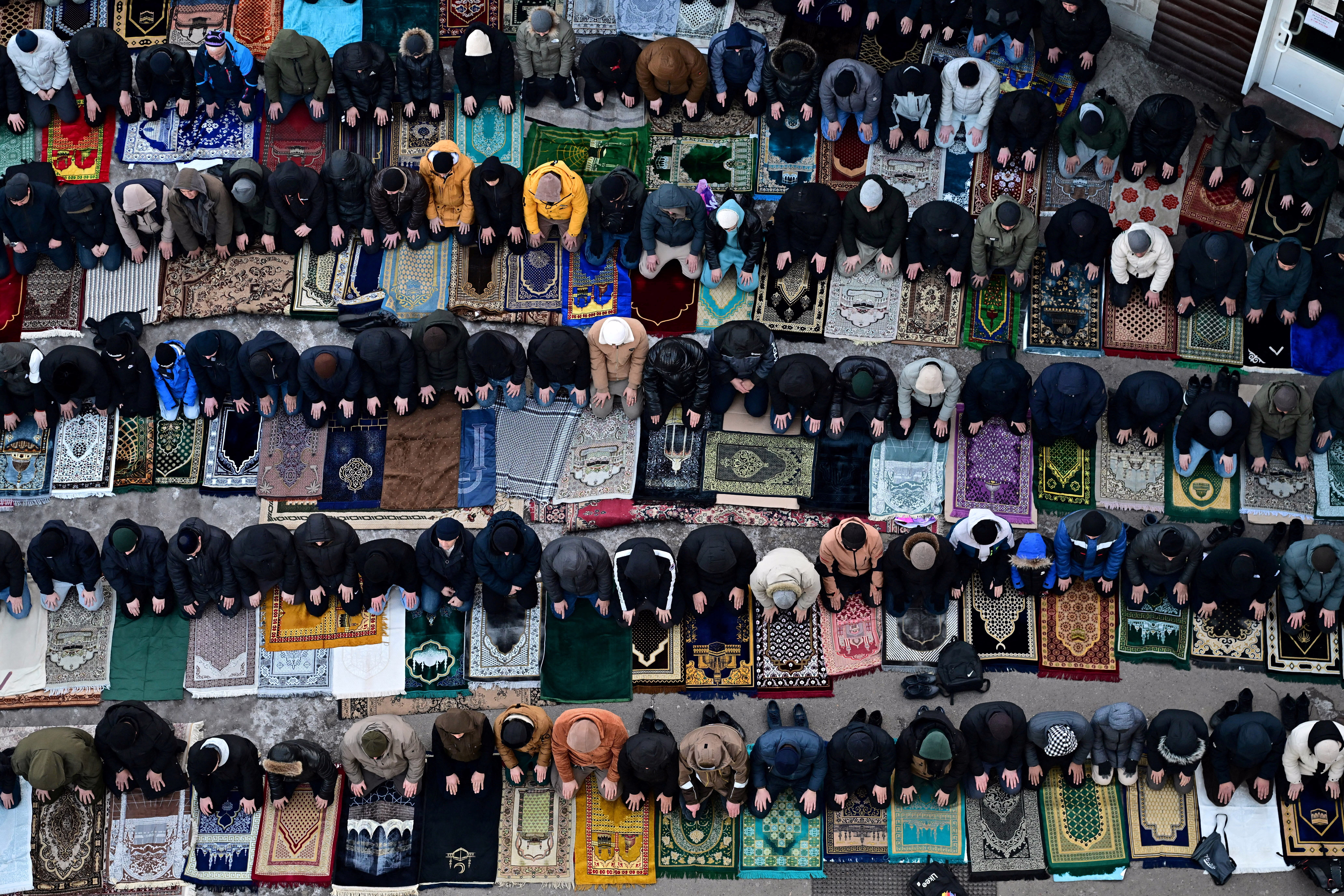 An aerial view of Muslim men kneeling on prayer mats arranged in rows.