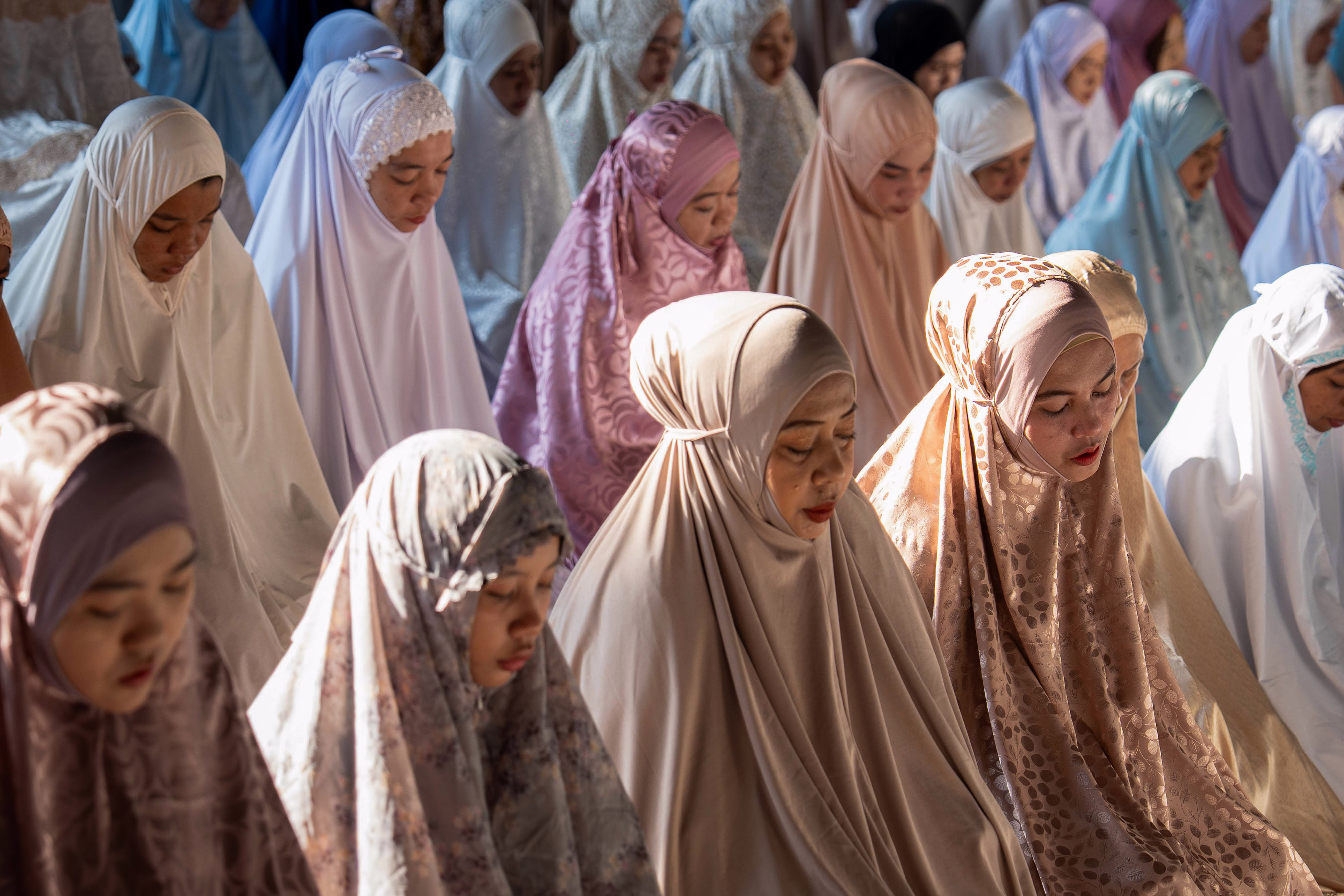 Women wearing different colored hijabs sit together during prayer.