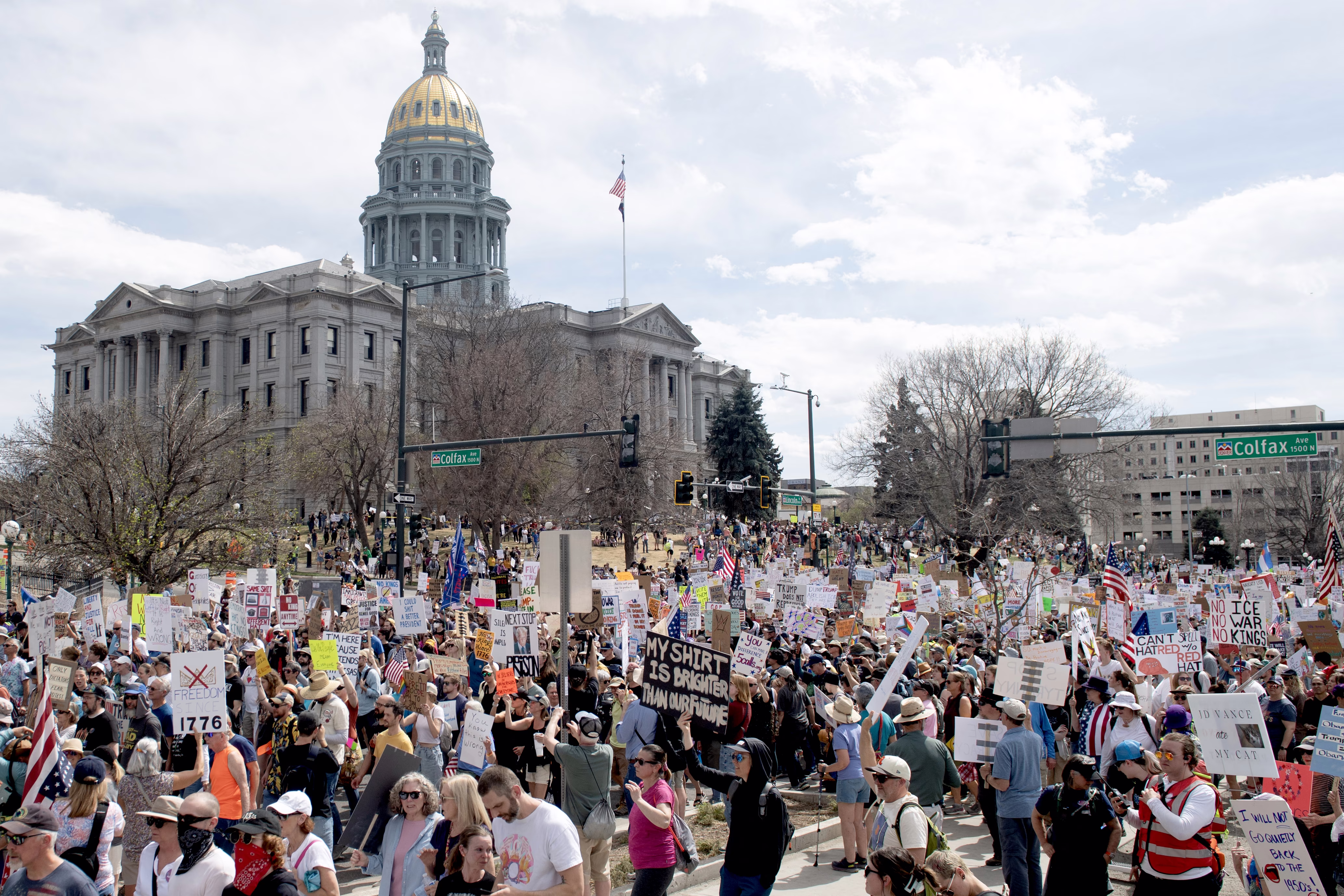 A large group of protesters marches outside a state capitol building.