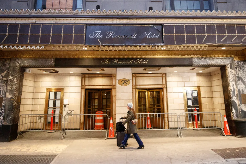 The exterior of The Roosevelt Hotel in NYC, with a woman walking past its ornate entrance.