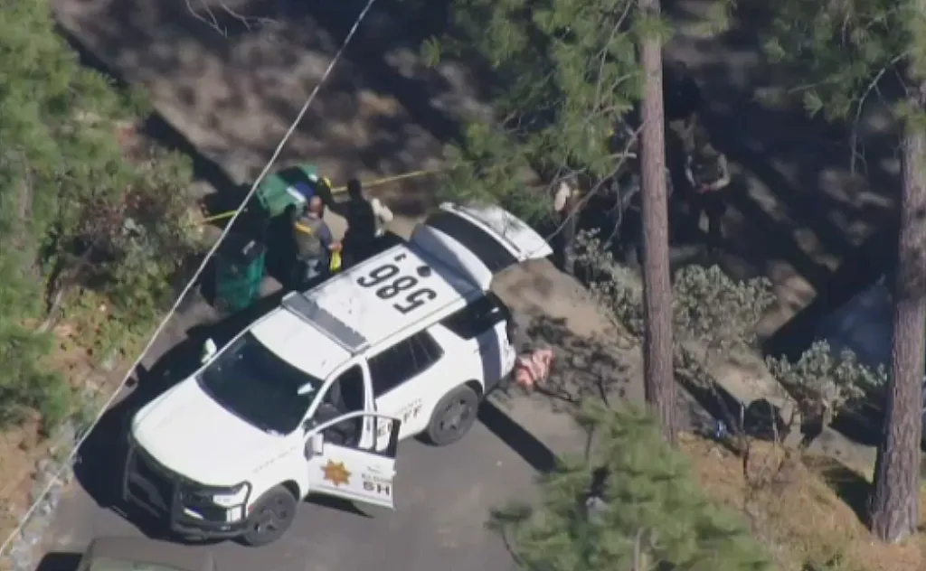 An aerial view shows a white El Dorado County Sheriff's vehicle with its doors open near people and a green bin, with caution tape visible.