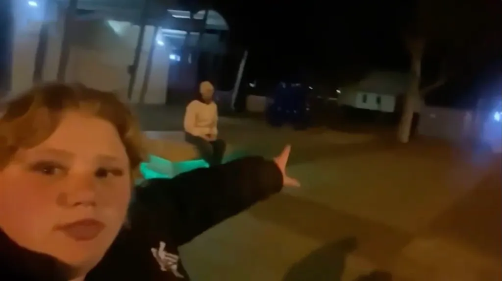 A woman pointing to a large blue sculpture in the dark.