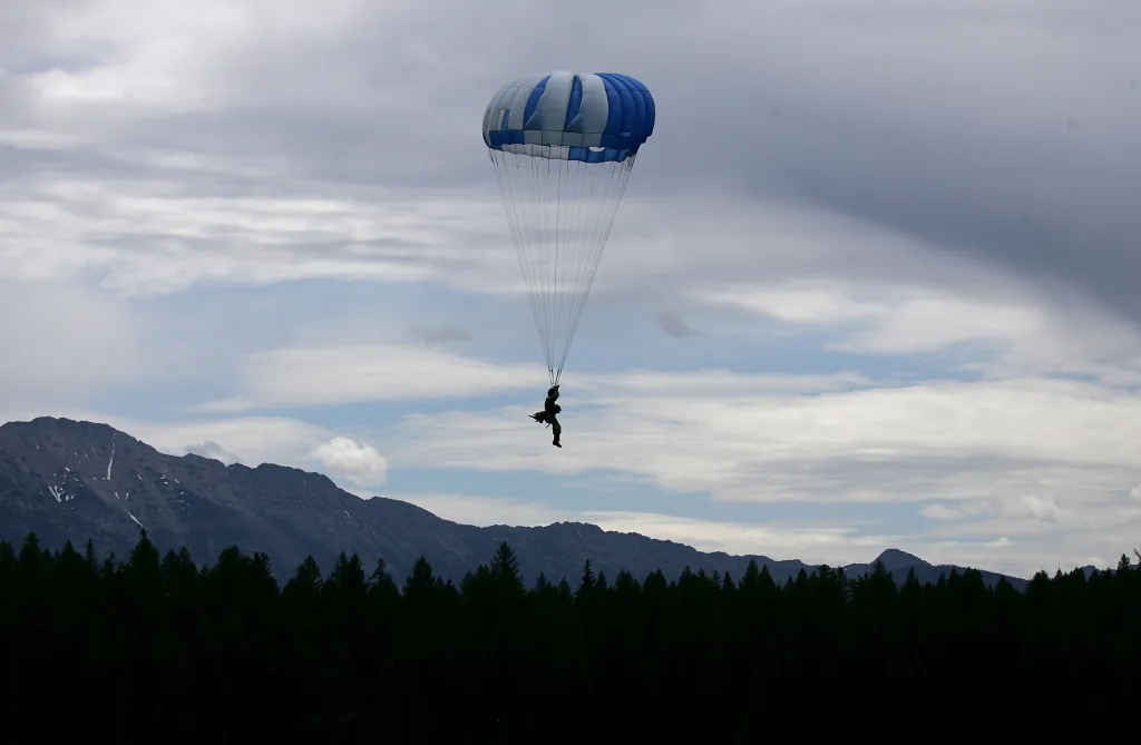 A rookie Smoke Jumper parachutes into Lake Lindbergh with mountains and a forest in the background.