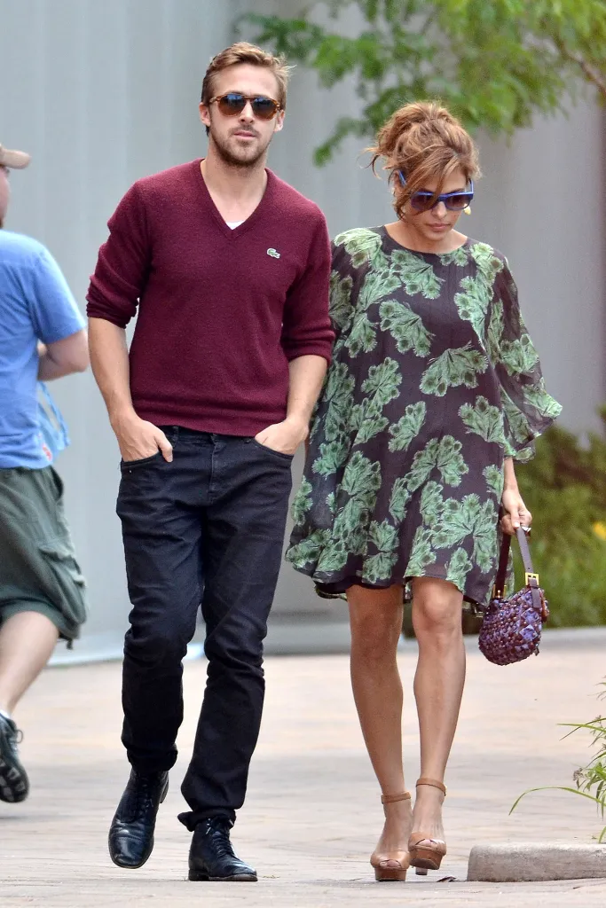 Eva Mendes and Ryan Gosling walking together, he wears a burgundy sweater and jeans, and she wears a green and black printed dress.