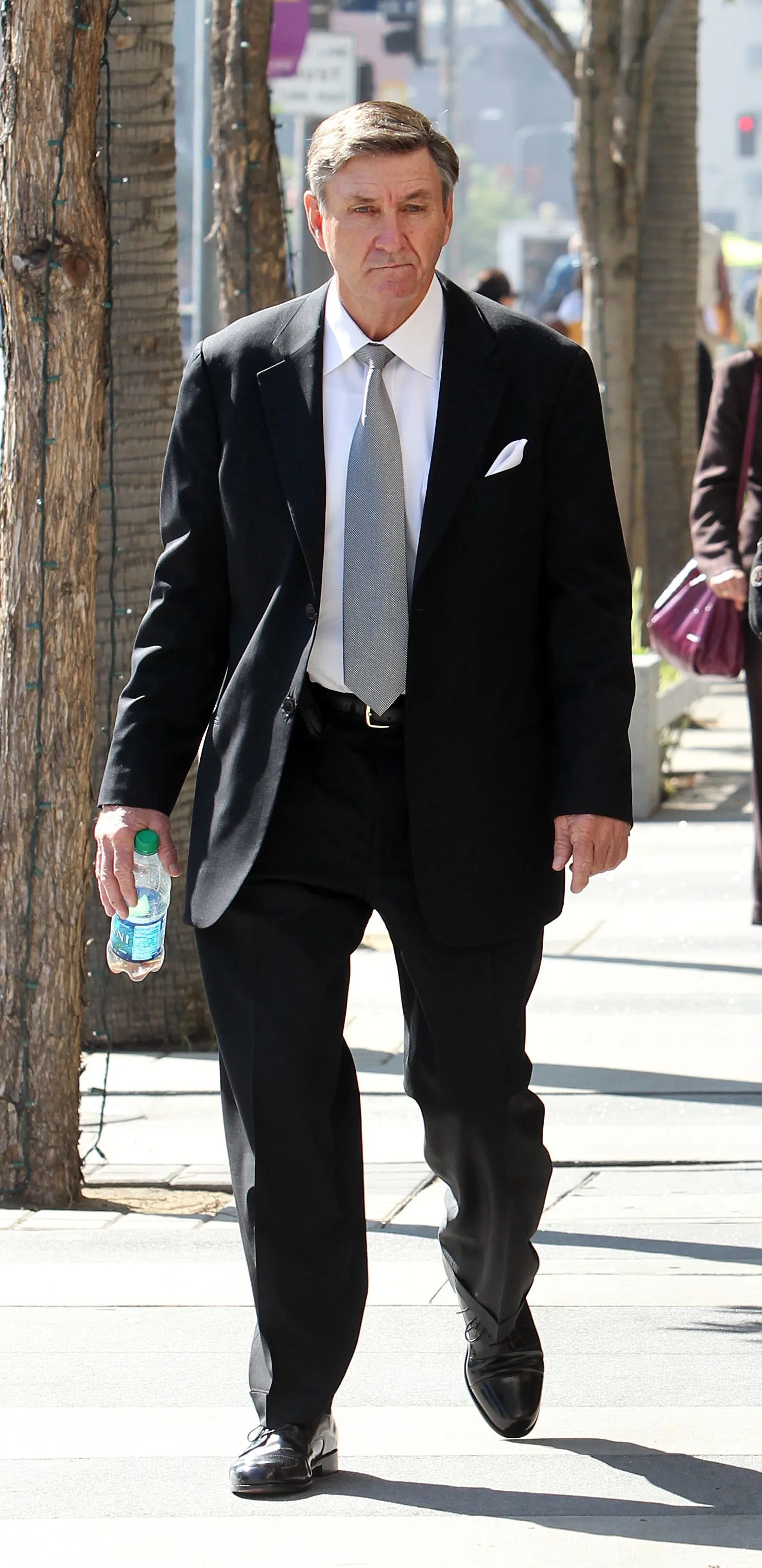 Jamie Spears in a suit, walking with a water bottle in hand.