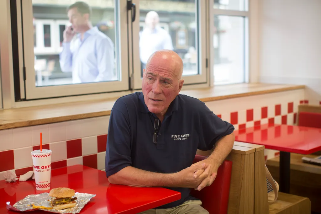 Jerry Murrell, founder of Five Guys, sits with a cheeseburger at a booth inside the company's new hamburger outlet in London.
