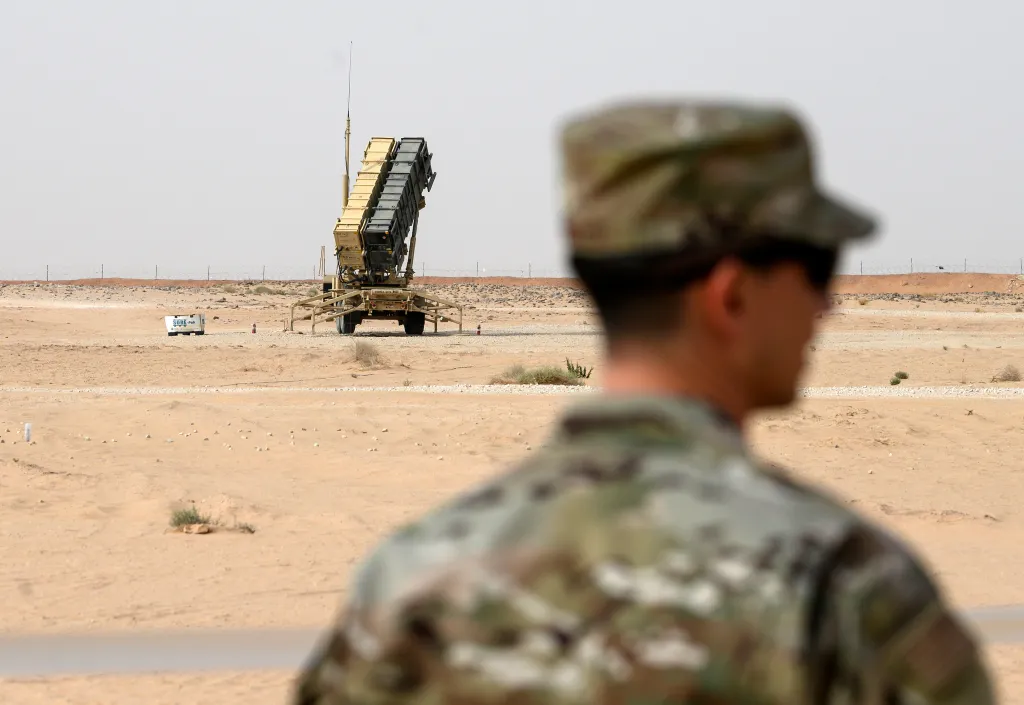A U.S. Air Force member in camouflage stands in the foreground, facing a Patriot missile battery at Prince Sultan Air Base in Saudi Arabia.