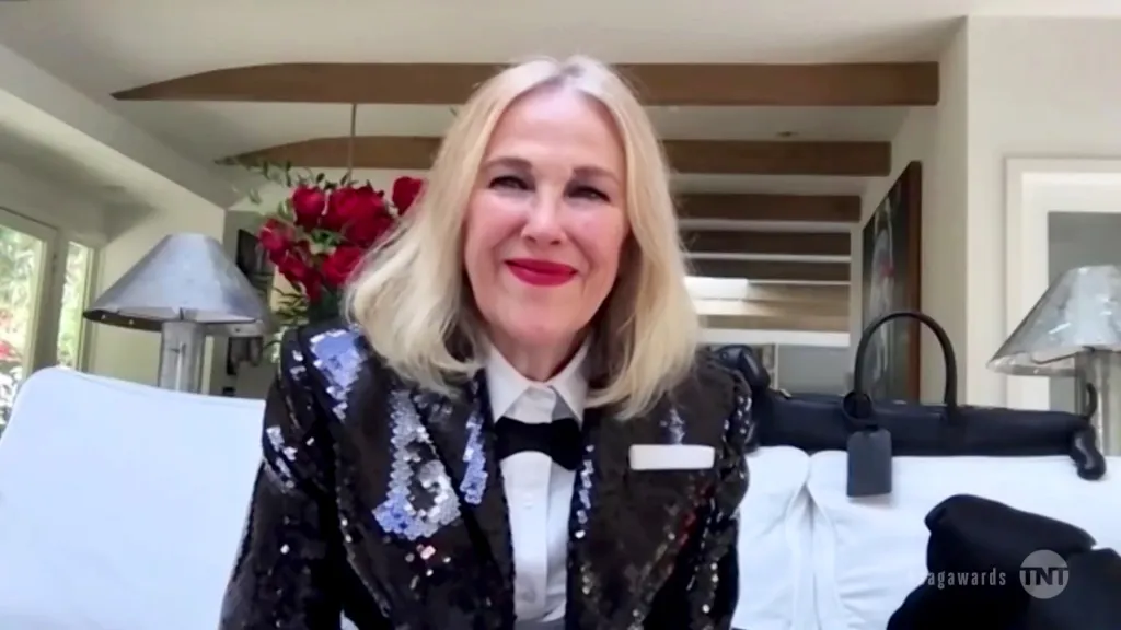 Catherine O'Hara smiles wearing a sequined black jacket over a white shirt and black bow tie.