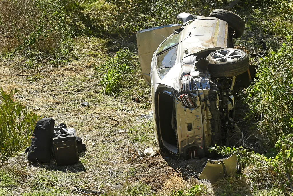 A silver SUV lies on its side in a ditch off the side of the road, having crashed.