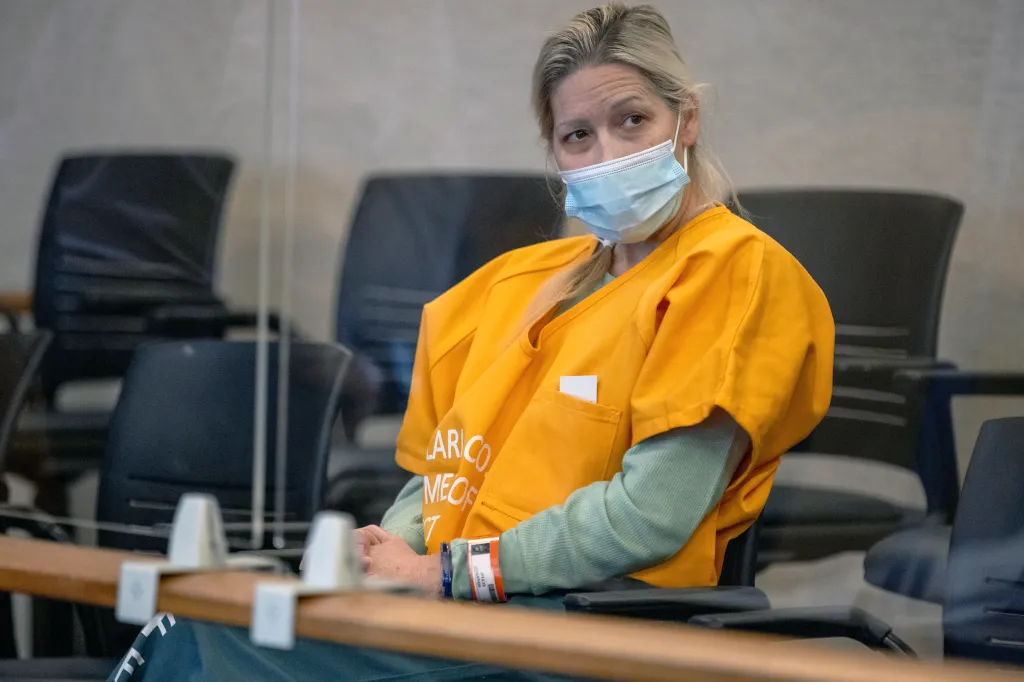 Shannon O'Connor, a blonde woman in an orange shirt and medical mask, listens in a courtroom.