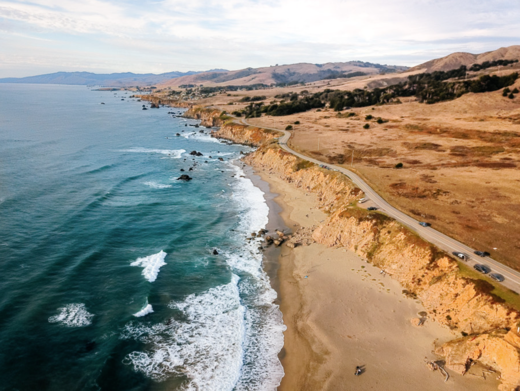 Aerial view of Salmon Creek Beach, showing a sandy coastline, crashing waves, and a road along the cliffside.