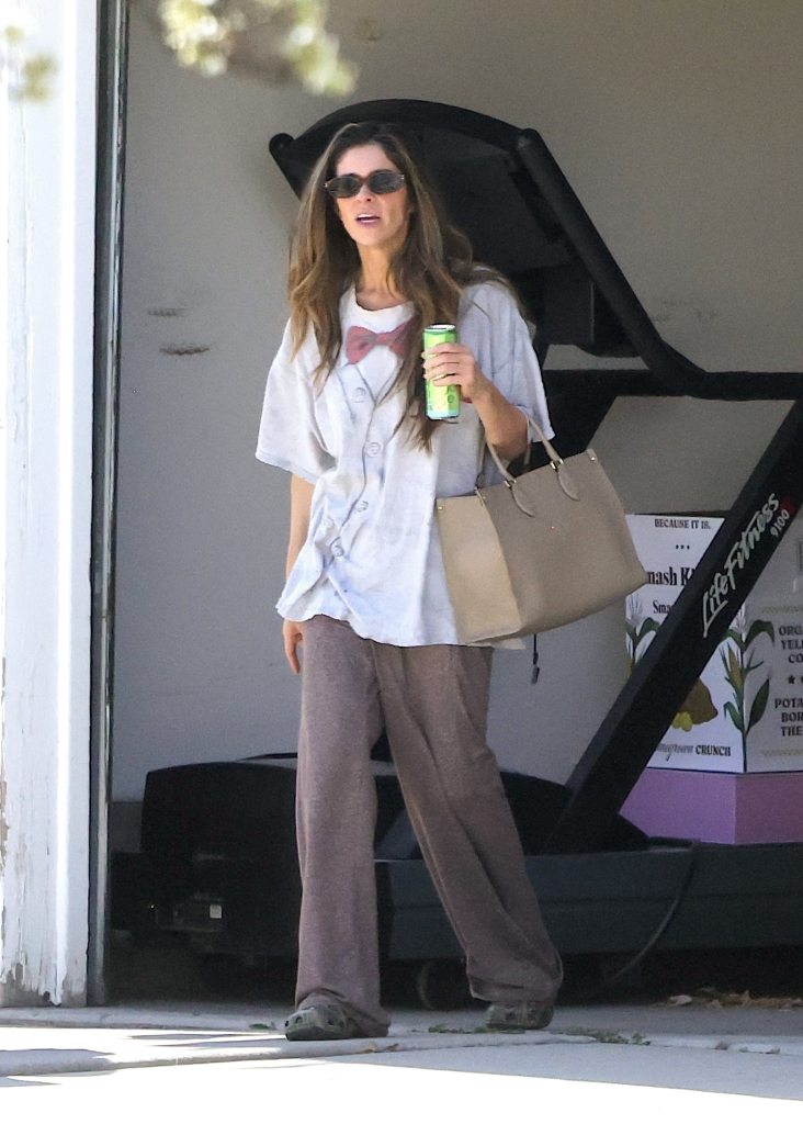 Taylor Frankie Paul in casual attire, wearing an oversized graphic t-shirt and wide-leg pants, holding a drink and a handbag.